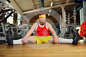 Fat funny man tired sitting on the floor in the gym