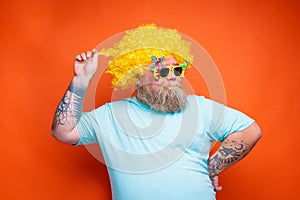 Fat happy man with beard, tattoos and sunglasses has fun with the yellow wig