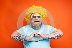 Fat happy man with beard, tattoos and sunglasses makes heart shape with hands