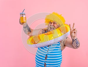 Fat happy man with wig in head is ready to swim with a donut lifesaver