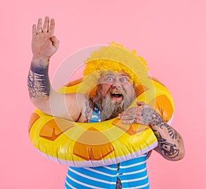 Fat happy man with wig in head is ready to swim with a donut lifesaver