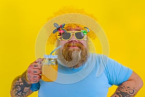 Fat happy man with wig in head and sunglasses drinks a fruit juice