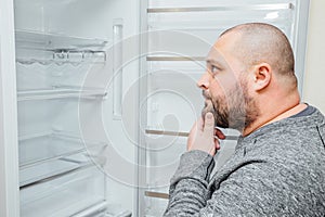 Fat hungry man is looking for a food into empty fridge