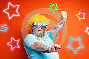 Fat man with beard, tattoos and sunglasses dances music on a disco
