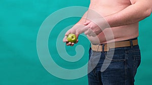 Fat man with a big belly holds a green apple and a banana in his hands. The concept of healthy eating and losing weight