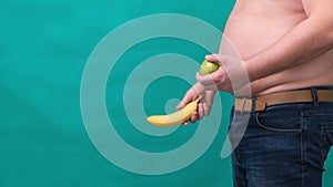 Fat man with a big belly holds a green apple in his hand. The concept of healthy eating and losing weight, diet.