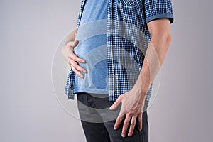 Fat man with bloating and abdominal pain, overweight male body on gray background photo