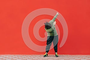 Fat man in casual clothes stands on a red background and dances a dab dance. Overweight guy shows dab movement in dance on red