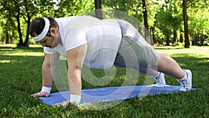 Fat man doing plank, training outdoors, desire to be slim, motivation willpower