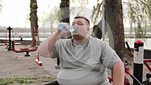 A fat man drinks water while exercising outdoors. Overweight man, weight loss concept