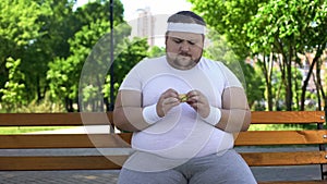 Fat man eating burger in park, addiction to junk food, unhealthy lifestyle