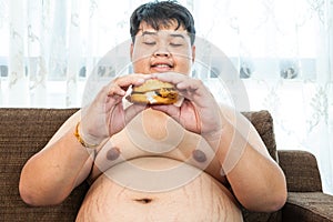 Fat man eating hamburger seated