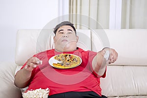 Fat man eating popcorns and holding remote control