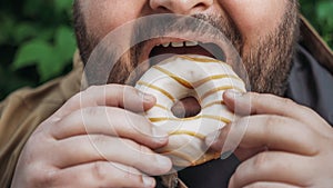 Fat man eats donut on street, close up. Unhealthy glazed sweet fast food