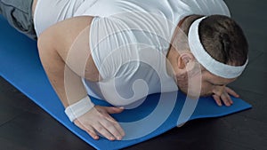 Fat man falling down on yoga mat trying to do plank exercise, lack of energy