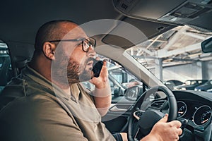 Fat man in glasses talking on cell phone while driving car in parking lot