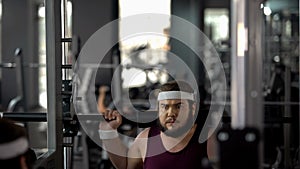 Fat man hardly doing exercise with barbell in gym, fitness workout, weight loss