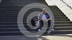 Fat man listening to music on stairs, loneliness, overweight causes insecurities