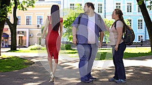 Fat man looking at beautiful lady in red passing by, obese girlfriend jealous