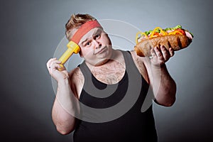 Fat man looking at camera and holding burger and dumbbell