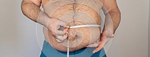 fat man measures the size of the abdomen with a centimeter measuring tape. person is overweight, he is obese.