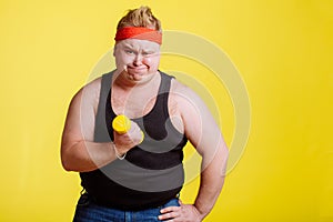 Fat man try to lift small yellow dambbell