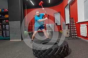 Fat man is very persistent training with sledgehammer and tire in the gym. Overweight