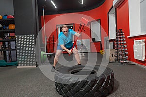 Fat man is very persistent training with sledgehammer and tire in the gym. Overweight