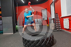 Fat man is very persistent training with sledgehammer and tire in the gym. Overweight