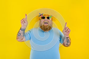 Fat man with wig in head and sunglasses indicates with hands something