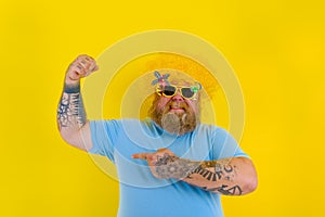 Fat man with wig in head and sunglasses shows his muscle