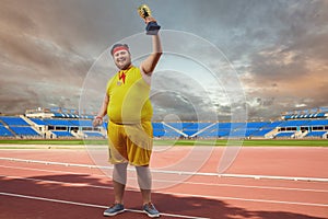 A fat man with a winner`s cup in his hands at the stadium.