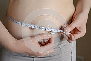 A fat obese woman measures her waist with a centimeter tape, close-up. Weight loss, obesity. Woman after childbirth.