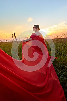 Fat plump chubby pleasant woman or girl in elegant red dres in green grass field. model posing outdoors on nature in a