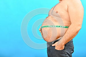 A fat and pot-bellied man with a large belly measures his waist with a centimeter