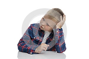 A fat, sad boy sits at a table with his head in his hands. Schoolboy in a plaid shirt. Back to school. Isolated on white
