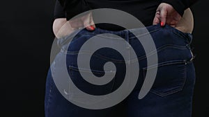 fat woman with cellulite trying to put on jeans on black background