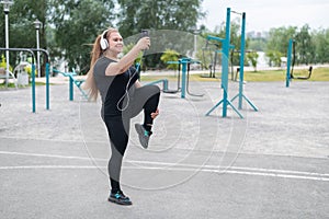 Fat woman doing sports outdoors and listening to music on smartphone.