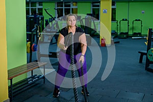 Fat woman doing strength training using battle ropes in the gym. An obese athlete moves the ropes in a wave motion to
