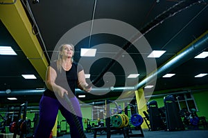 Fat woman doing strength training using battle ropes in the gym. An obese athlete moves the ropes in a wave motion to