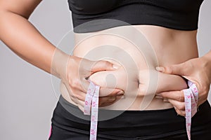 Fat woman hand holding excessive belly fat with measuring tape. Healthcare and woman diet lifestyle concept to reduce belly and