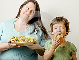 Fat woman holding salad and little cute boy with hamburger