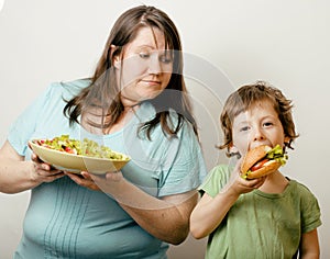 Fat woman holding salad and little cute boy with hamburger