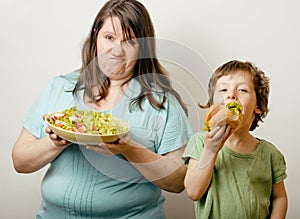 Fat woman holding salad and little cute boy with hamburger