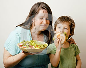 Fat woman holding salad and little cute boy with hamburger