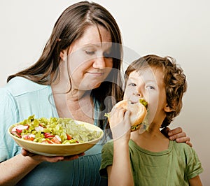 Fat woman holding salad and little cute boy with hamburger