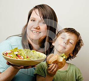 Fat woman holding salad and little cute boy with hamburger