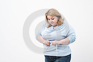 A fat woman measures her waist with a measuring tape in casual clothing on a white background.