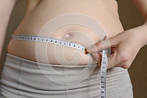 A fat woman measures her waist with a measuring tape, close-up.Lifestyle, diet concept.