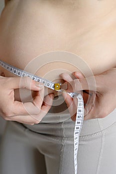 A fat woman measures her waist with a measuring tape, close-up.Weight loss, obesity. Woman after childbirth.